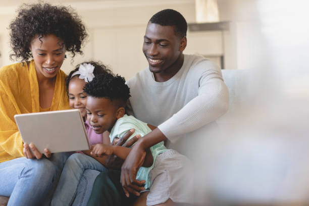 istock Happy African American parents with their cute children using digital tablet on sofa 1129665147