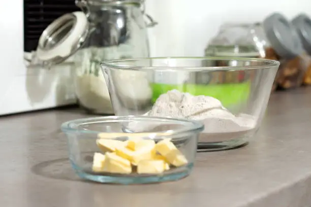 Preparation of ingredients for baking cakes. Butter and flour in glass containers stand on the kitchen counter.