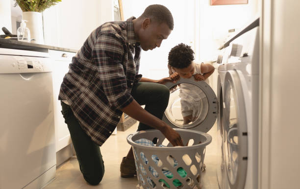 istock Father and son washing clothes in washing machine 1129667981