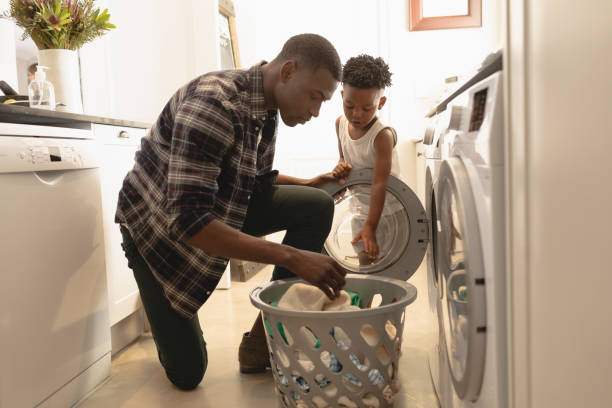 istock Father and son washing clothes in washing machine 1129668032