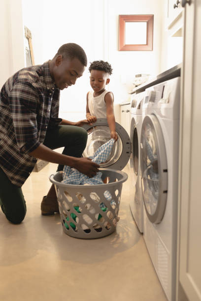 istock Father and son washing clothes in washing machine 1129668064