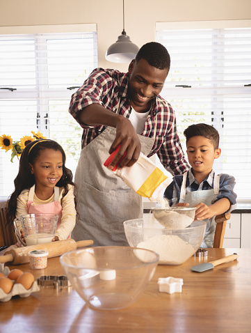 Front view of African American father and children baking cookies in kitchen at home