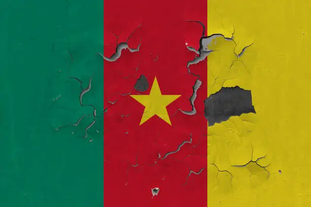 Photo of Close up grungy, damaged and weathered Cameroon flag on wall peeling off paint to see inside surface.