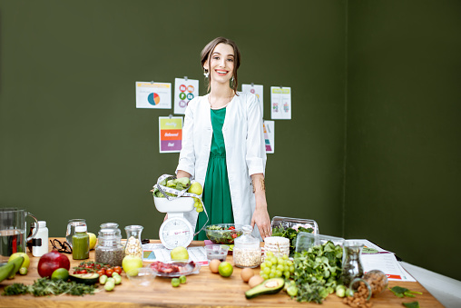 Portrait of a young woman nutritionist standing near the table full of healthy products in the green office