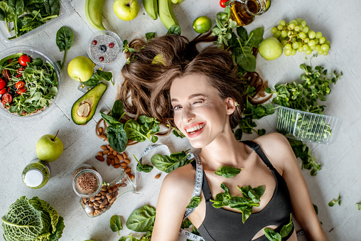 Beauty portrait of a woman surrounded by various healthy food lying on the floor. Healthy eating and sports lifestyle concept