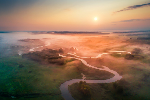 Germany. Spring colorful landscape. Green meadow with mist and river aerial drone view. Bright sun paints fog with red and yellow colors.