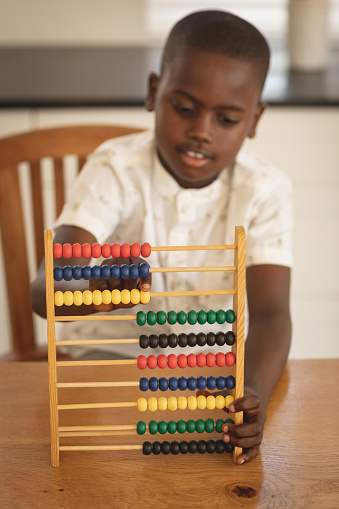 Front view of African American boy learning mathematics with abacus on dining table in kitchen at home