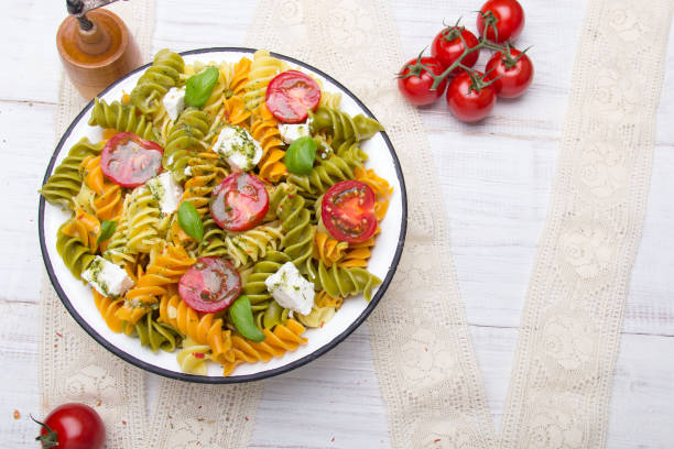 Italian food - Salad with colorful pasta, cherry tomatoes, feta cheese and fresh basil on white wooden background
