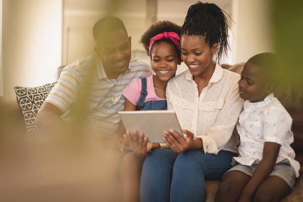 istock Happy African American family sitting on the sofa and using digital tablet 1129675580