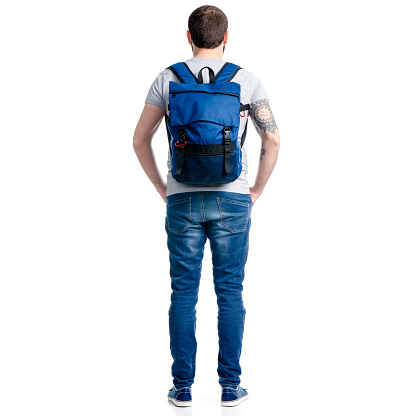 A man tourist in jeans with blue backpack standing looking on white background isolation, back view