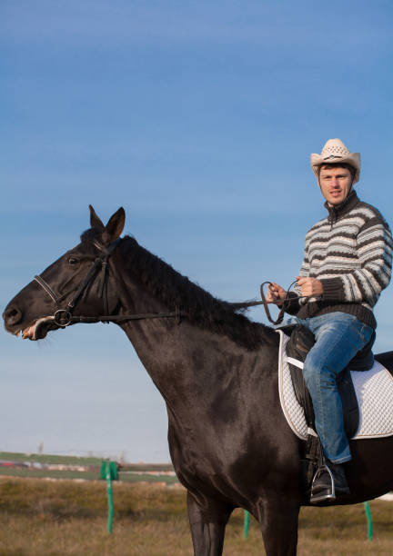 istock Man riding horse, striped pullover, blue jeans, hat, close up 1129679814