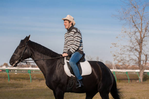 istock Man riding horse, striped pullover, blue jeans, hat, close up 1129680469