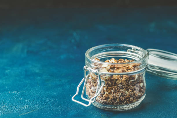 istock Open glass jar of organic granola on a dark blue concrete table 1129684219