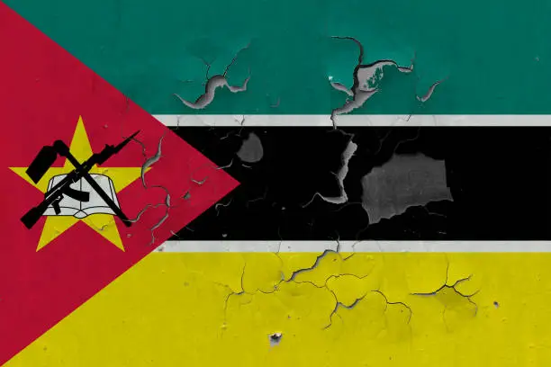 Photo of Close up grungy, damaged and weathered Mozambique flag on wall peeling off paint to see inside surface.