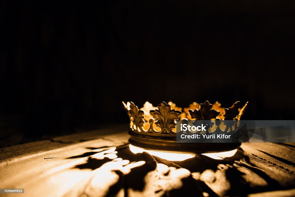 Crown of the real king on a black background. Game of Thrones. The crown on a black background is highlighted by a golden ray. Game of Thrones. Crown - Headwear Stock Photo