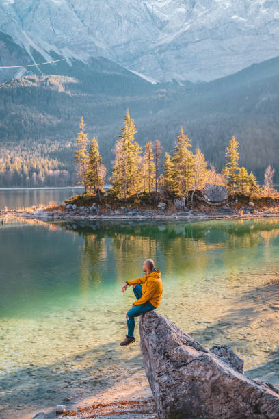 What a day to be alive Photo of Traveler Man relaxing meditation with serene view mountains and lake landscape Travel Lifestyle hiking concept summer vacations outdoor. Male dreamer, sitting on the Ibsen lake edge in Germany at sunset, human strength, psychology concept. Men Wearing Jacket sitting on rock during autumn day and looking away. zugspitze mountain stock pictures, royalty-free photos & images