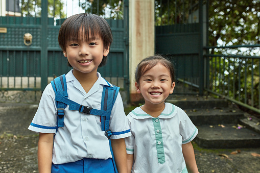 Portrait of cute siblings standing outside house. Happy brother and sister are going to school. They are wearing uniforms.