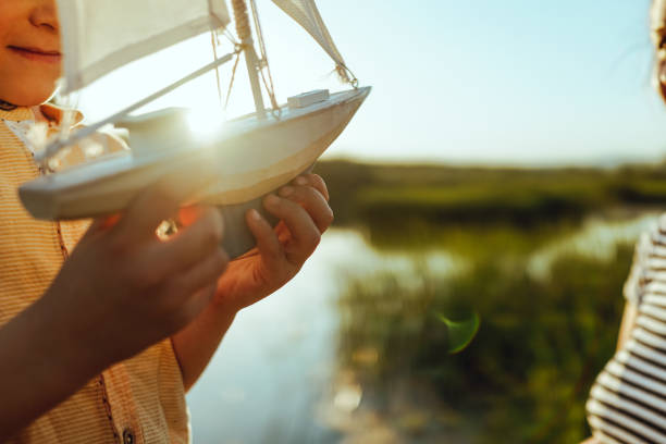 Little boy by the lake holding a toy boat.