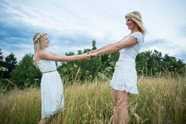 Females in the nature enjoying life, dancing in grass, holding hands with floral garland in heads.