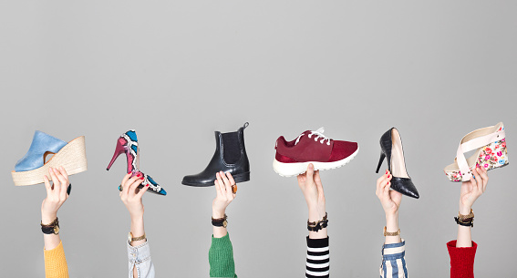 Hands holding different shoes on gray background