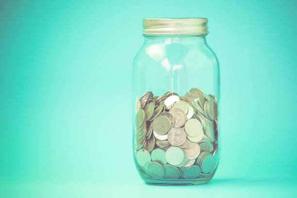 istock Close-Up Of Coins In Jar Against Blue Background 1129702449