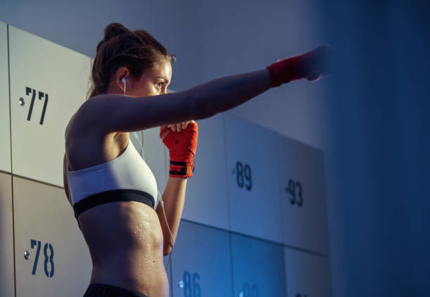 istock Young sportswoman warming up for kickboxing training in gym's dressing room. 1129703888