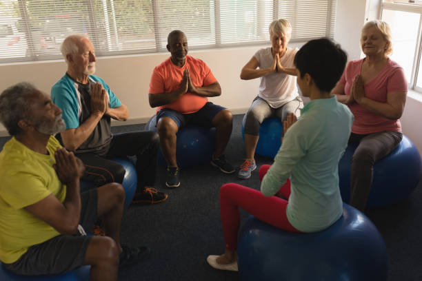 weibliche trainer training senioren bei der durchführung von yoga - senior adult exercising aging process instructor stock-fotos und bilder
