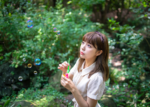 Young woman looking at soap bubbles in forest