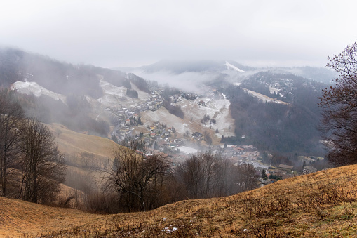 Misty mountain valley with snow and fog. Evocative fantasy landscape in the mist with village.