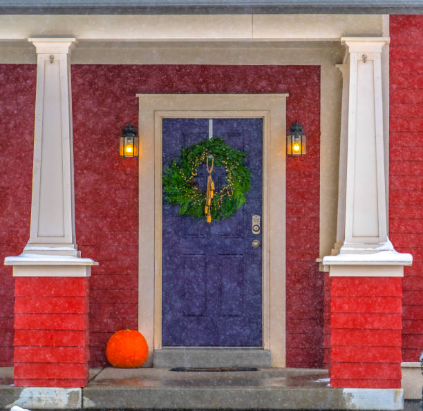 Facade of home in Utah seen through falling snow. Facade of a colorful home in Daybreak, Utah seen through falling snow. A leafy wreath with gold accents hangs on the vibrant blue front door.