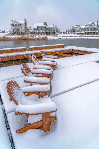 istock Snowy chairs on lake deck with view of homes 1129745491