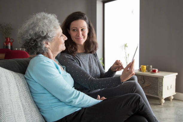 istock Smiling senior woman and her daughter using tablet computer 1129748694