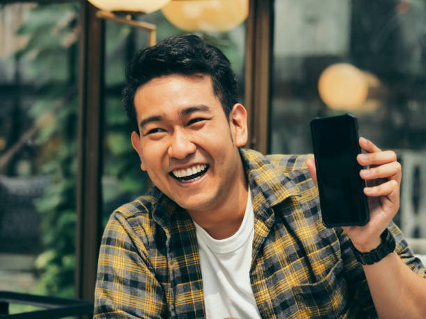 istock Happy Asian man pointing to black smart phone in his hand. 1129764889