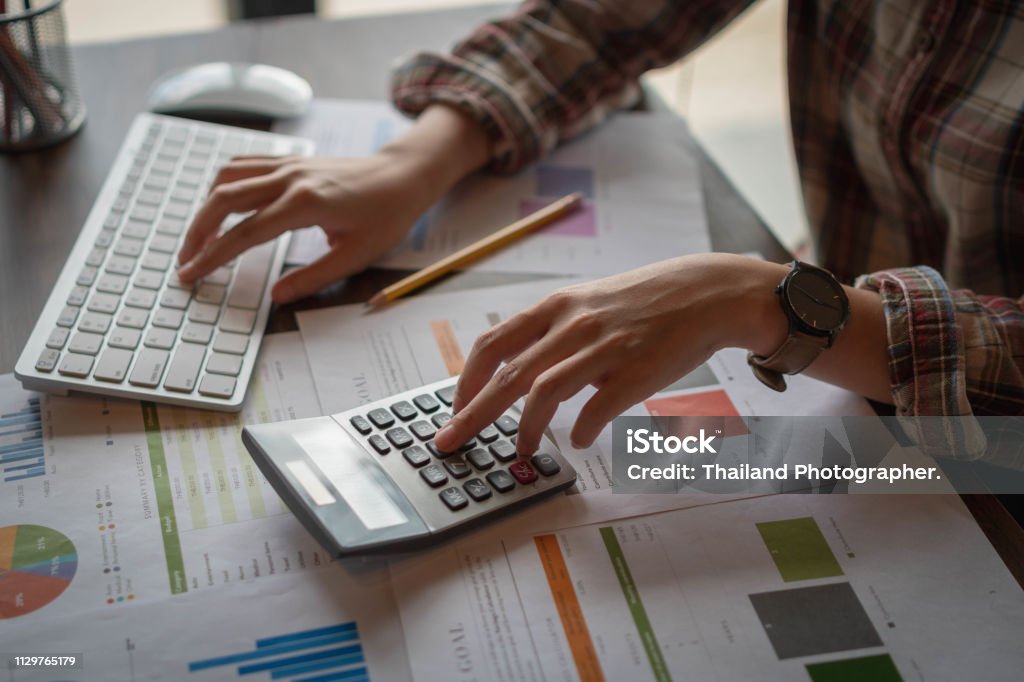 Businesswoman analyzing financial reports with calculator and  typing on modern computer keyboard at office. Business analytics concept. Accounting and technology in office. Accountancy Stock Photo