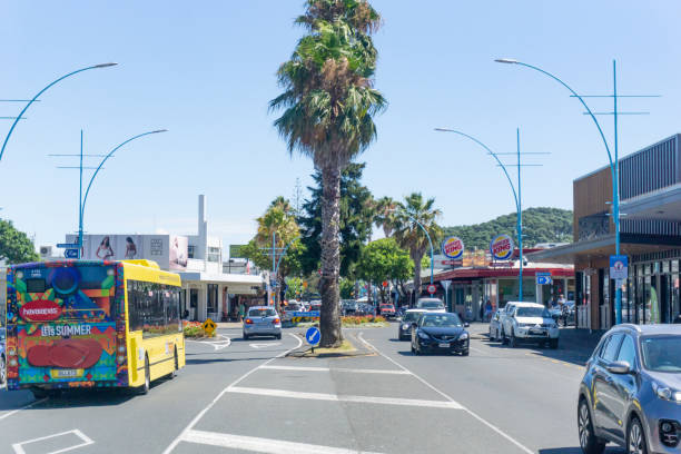 Maunganui Road in main shopping area with passing vehicles and people, Maunganui Road in main shopping area with passing vehicles, yellow bus and people  in February 2019 at Mount Maunganui New Zealand tauranga new zealand stock pictures, royalty-free photos & images