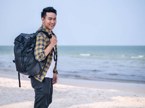 istock Happy Asian man wih backpack standing at the beach. 1129777862