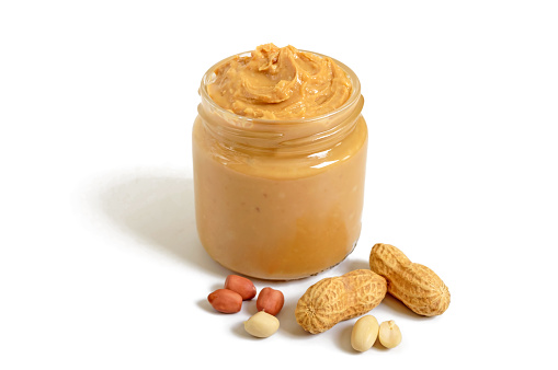 Peanut butter in a glass jar with peanuts isolated on white background.  A traditional product of American cuisine.