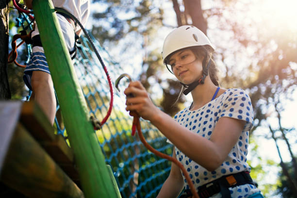 Kids during ropes course in and adventure park. The girl is attaching a carabiner.Sunny summer day.Nikon D850