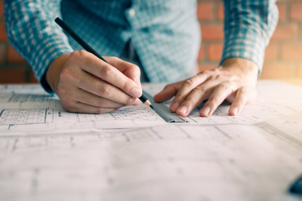 istock Engineering or architect reviewing blueprints and holding pencil on desk at home office. 1129789140