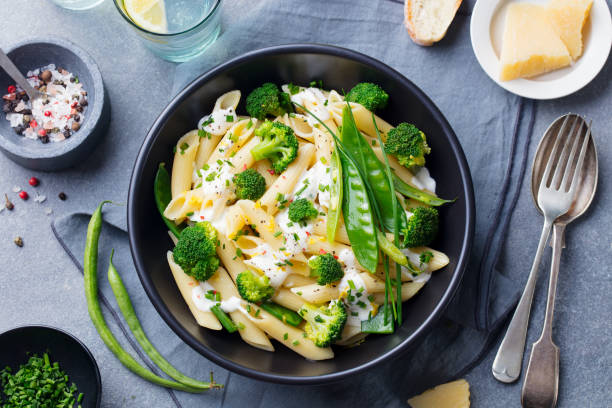 Pasta with green vegetables and creamy sauce in black bowl on grey stone background. Top view. Pasta with green vegetables and creamy sauce in black bowl on grey stone background. Top view penne stock pictures, royalty-free photos & images