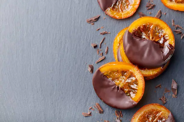 Photo of Candied orange slices in chocolate. Slate background. Top view. Copy space.