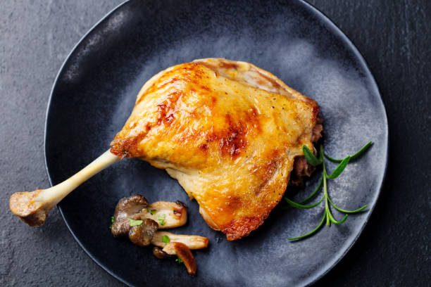 istock Duck leg confit with mushroom sauce on black plate. Stone background. Close up. 1129797328