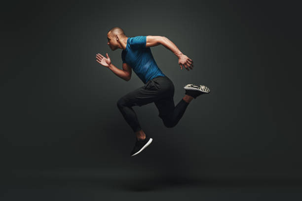 Jump higher Sportsman jumping over dark background Full length portrait of a healthy muscular sportsman jumping isolated over dark background. Dynamic movement. Side view sportsman professional sport side view horizontal stock pictures, royalty-free photos & images