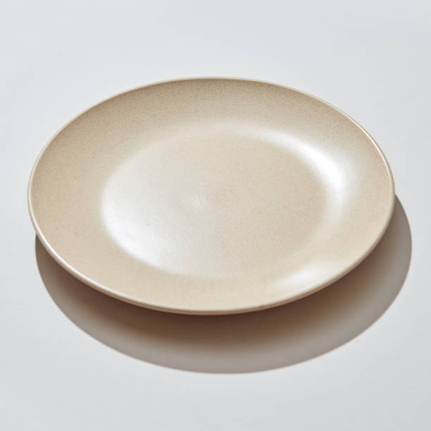 istock Porcelain handmade empty plate in a pastel color on a gray background with shadows. 1129801110