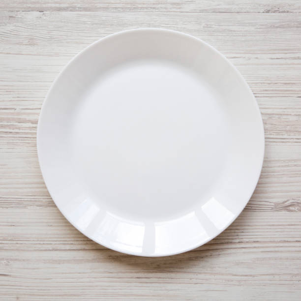 istock White plate on white wooden table, top view. Flat lay, overhead, from above. 1129801343