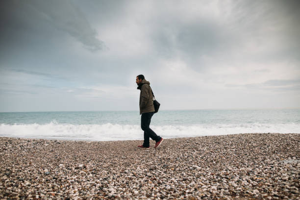 istock Man walking on the beach on rainy day 1129805300