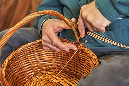Detail shot focusing on the hands of a weaver as they create a woven basket, emphasizing the precision of the craft.