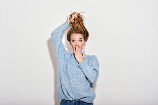 What a surprise! Cute lady is shocked. She holds her hair and covers her open mouth with palm. Looking at camera isolated over white background Portrait of sweet, gorgeous, stunning, adorable lady with staring eyes, holding her nice brown hair, while covering her open mouth with palm, , standing isolated over white background vogue cover stock pictures, royalty-free photos & images