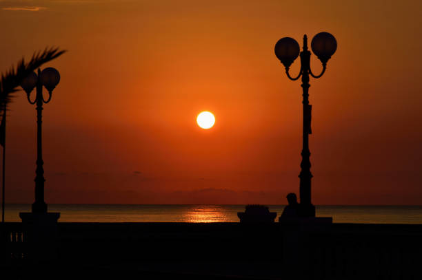 Sunset over the sea calabria, italy - August 5, 2015. image of the sea at sunset. The sun is a red sphere. in the foreground silhouettes of two lamps not illuminated and a bench cielo minaccioso stock pictures, royalty-free photos & images
