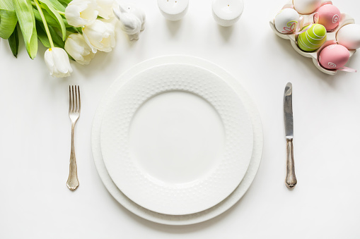 Easter dinner. Table setting with white tulip, colorful eggs on white table. Top view. Space for text.
